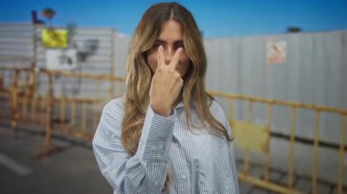 Sarı saçlı kadın inşaat alanında V işareti işareti gösteriyor; kendine güvensizlik kararlılığı güçlendirme.