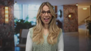 Sarı saçlı ve gözlüklü bir kadın otel lobisinde el ele tutuşuyor..