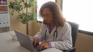 Kadın doktor telefonu kulağına tutarken steteskopla klinik masasına dizüstü bilgisayar ve dosyalarla sarılmış..