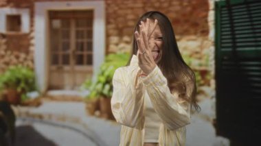 Kadın yüzünü eliyle kapatıyor ve binanın girişinde dili dışarı çıkıyor, rahat gömleğiyle gülümsüyor; neşeli bir an..