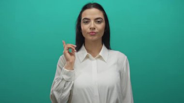 Katı yeşil bir arkaplan önünde beyaz bir gömlek giyerken bana el kol hareketi yapan bir kadın görüntüye dostça ve davetkar bir hava katıyor..