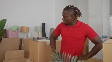 Kalça üzerinde duran bir adam taşınmak için paketlenmiş evde karton kutuya dokunuyor; taşınma günü belirleme.