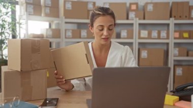 Paket ve dizüstü bilgisayar taşıyan kadın, ilk pompa jesti ve raflar dolusu nakliye kutuları; küçük işletme başarısı neşe.