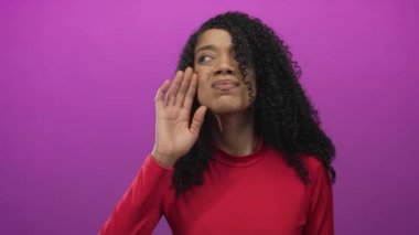 Kırmızı tişörtlü, kıvırcık saçlı bir kadın mor stüdyoda el ele tutuşuyor..