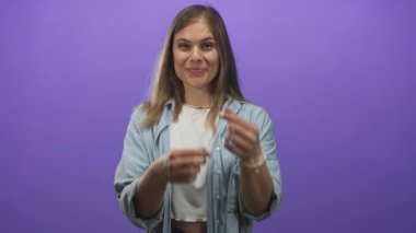 Kot gömlek giyen sarışın kadın stüdyoda gülümserken parmak kalp hareketi gösteriyor..