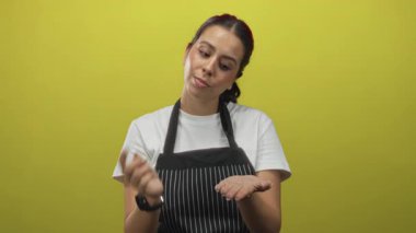 Çizgili önlüklü genç esmer kadın sarı arka planda açık bir el tutarken avuç içini ovuyor ve parmaklarını çimdikliyor; konsantrasyon becerisi.