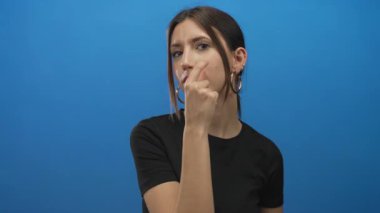 Mavi bir stüdyoda dudaklarıyla dudaklarına dokunan İspanyol genç kadın, sessiz sakin içgözlem farkındalığı.