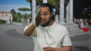 Adam işaret parmağı uzatılmış taş anıtın yanındaki sokakta kamerayı işaret ediyor; harekete geçme sürprizi çağrısı.