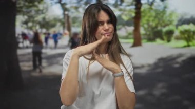 Çevresi canlı yeşilliklerle çevriliyken parkta mola veren genç İspanyol kadın ve arka plandaki bulanık insanlar boş zamanlarını ve rahatlamayı aktarıyor..