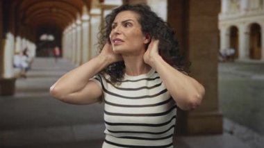 Kadın kulaklarını güneş ışığıyla kaplı tarihi bina koridoruyla kapatıyor. Gürültü kirliliği stresi..