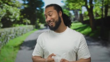 Elleri göğsünde, orman yolunda gülümseyen, beyaz tişört giyen, sakallı, yeşil parktaki at kuyruklu adam, minnettarlık..