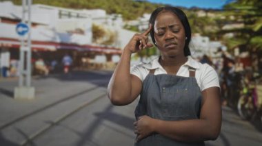 Kot önlüklü kadın, diğer elini karnında tutarken şakağına işaret ediyor. Düşünceli bir karar..
