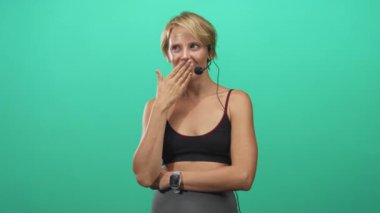 Siyah spor sutyenli ve akıllı kadın yeşil stüdyoda kulaklık takarken ağızlarını eliyle kapatıyor; şakacı utangaçlık.