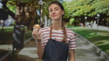Eldivenli eldiveni olan ve sokak yolunda ağaçların ve lamba direklerinin yanında önlük ve çizgili gömlek giyerken parmak yanağa gezen kadın..