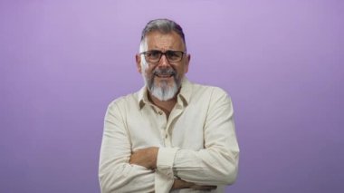 Orta yaşlı bir adam stüdyoda mor arka plana karşı çıplak elle orta parmaklarını gösteriyor, gözlük ve keten gömlek takıyor, meydan okuyor..