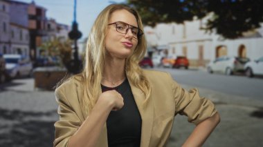 Güneşli bir şehir caddesinde kendine güveni tam bir şekilde el kol hareketi yapan bir kadın, kentin dış ortamında kendine güvenini ve duruşunu ifade ediyor..