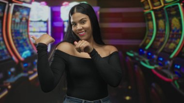 Genç Latin kadın kumarhanedeki parlak kumar makinelerinin önünde duruyor ve makine ekranındaki başparmaklar; şans heyecanı.