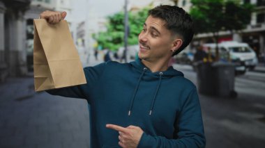 Elinde bir kese kâğıdı tutan genç adam hareketli bir şehir caddesinde, şehir geçmişi ve yakındaki yayaları olan sıradan bir şehir hayatı sergiliyor..