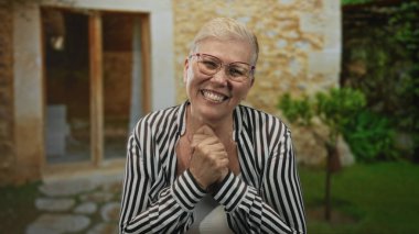 Elleri göğsüne yapışan bir kadın bina girişinde hafifçe öne eğilerek gülümserken; minnettarlık bağı konforu.