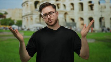 Roma 'da kolezyumun önünde ellerine bakan sakallı genç bir adam. Roma' nın ikonik Roma ortamında düşünceli ve kararsız görünüyor..