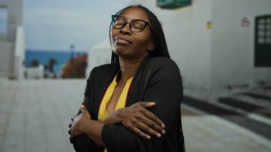 Kadın kentin sokaklarında kendini kucaklıyor, modern gözlüklerden ve güneşli gökyüzünün altında gündelik kıyafetlerden tatmin ve sakinliğini ifade ediyor..