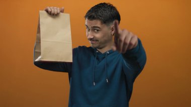 İzole edilmiş turuncu arka planda kameraya işaret eden İspanyol genç adam nişan ve etkileşim öneriyor.