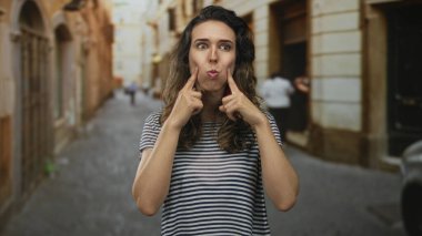 Güneşli, eski bir kasaba caddesine parmaklarını uzatan kadın tuhaf bir ifadeyle, şakacı bir yaramazlık yapıyor..