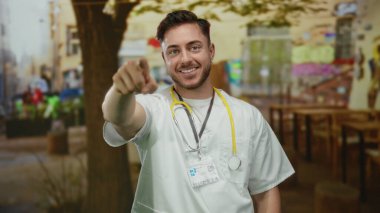 Sakallı ve steteskoplu beyaz bir erkek doktor gülümsüyor ve bir restoran sokağının terasına işaret ediyor..