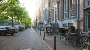 Bisikletler ve arabalarla dolu büyüleyici bir caddenin odak dışı görüntüsü, sıcak bir gün ışığı altında tarihi mimariyi ve canlı şehir atmosferini vurguluyor..