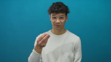 Gözlüklü genç adam stüdyo ortamında beyaz gömlek giyerek parmak hareketi yapıyor..