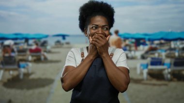 Deniz kenarındaki önlüklü kadın, elleri mavi şemsiyelerin altında ve açık gökyüzünde açık havada doğal bir anı yakalıyor..