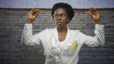 Kadın doktor her iki elini de steteskop ve gözlüklerle kaldırarak stüdyo tuğlasından duvar, sarı steteskop ve cep kalemlerini görünür hale getiriyor..