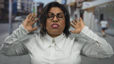 Şehir sokaklarında gözlüklü Latin bir kadın şehir ortamında hayal kırıklığına uğramış görünüyor..