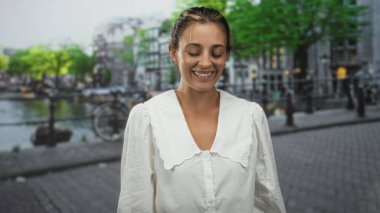 Amsterdam 'da sokakta yüzünü ve beyaz bluzunu gösteren yüzü kapalı gülümseyen kadın; memnuniyet yolculuk hafızası.