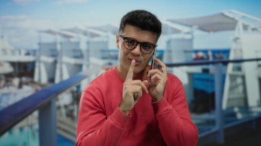 Gözlüklü genç adam akıllı bir telefonla konuşurken yolcu gemisinde gülümsüyor açık deniz manzarası ve rahat atmosferin tadını çıkarıyor..