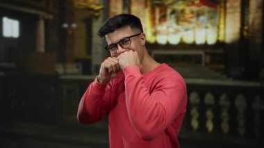 Gözlüklü genç adam kilisenin arka planında neşeli bir şekilde gülümsüyor. Neşeli ve sıradan bir ortam izlenimi veriyor..