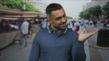 Şehir sahnesinin ortasında, işlek cadde pazarında üç parmağını gösteren genç adam eli; oyuncu bir güven.