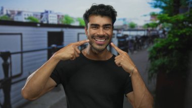 Parmakla gösterilen ve parmaklıklarla dolu kalabalık bir caddede geniş bir gülümseme; mutluluk..