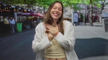 Göğüs göğüse gülümseyen genç İspanyol kadın, sokakta beyaz gömlek ve sarı tank giyiyor; minnettarlık sıcaklığı bağlantısı.