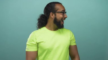 Sakallı ve gözlüklü bir adam stüdyoda gülümsüyor ve yüzü donuk yeşil gömlekli ve kıvırcık at kuyruklu bir adam..