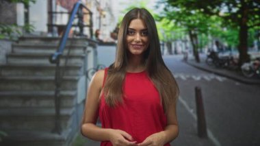 Elleri kolları bağlı, kırmızı kolsuz bir bluzla sokakta duran, kendine güvenen bir kadın..