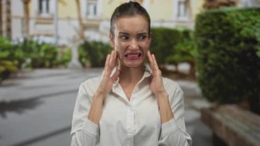 Beyaz gömlekli genç İspanyol kadın binanın ön cephesinde göğsüne yakın yumruklarını sıkıyor..