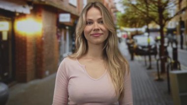 Sarışın kadın dar şehir caddesinde göğüs hizasında avuçlarını birbirine bastırıyor..