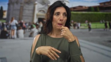 Kalabalık bir turizm meydanında çıplak çeneli bir kadın, eğik bir kuleye dokunuyor..