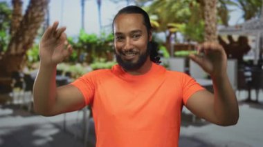 Açık hava restoranının terasında açık turuncu gömlekli bir adam var. Konukseverliği onaylıyor..