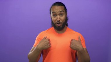 Göğsünü gösteren sakallı adam ve mor stüdyoda yumruklarını kaldıran turuncu tişört giyen, geniş gülümsemeli, zafer başarısı neşesi.