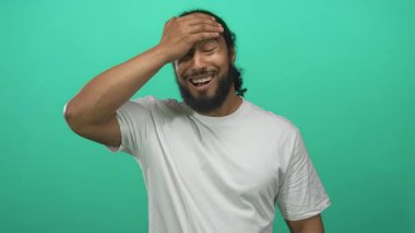 Stüdyoda parlak yeşil arkaplan karşısında acı çeken alnını gösteren bir adam var..