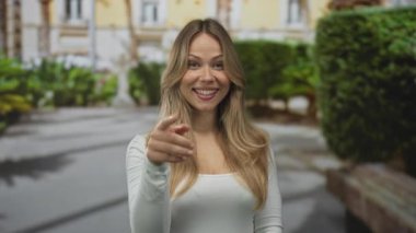 Kadın, kent caddesinde gülümserken iki elini de havaya kaldırır; davet sıcaklığı bağlantısına hoş geldin der.