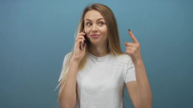 Mavi arka planda akıllı telefondan konuşan bir kadın, beyaz bir gömlek giyerken kafasını işaret ederek şaşkınlığını dile getiriyor..