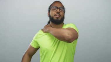 Yoğun idman sonrası gri stüdyoda neon yeşil gömlek giyerken omzunu tutan ve irkilen bir adam..
